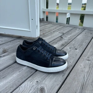 Mörkblå sneakers från Lanvin uk 10 passar 44/45 - Snygga mörkblå sneakers från Lanvin med ovandel i mocka och lackad tå. Skorna har vita sulor, rund tå och klassisk snörning. Perfekta för dig som gillar stilrena och exklusiva sneakers med en twist.