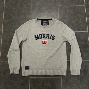 Morris stickad långarmad - Snygg grå tröja från Morris med broderad text och en Union Jack-flagga på bröstet. Tröjan har en rund halsringning och ribbade muddar vid ärmslut och nederkant. Perfekt för en stilren och avslappnad look. Jättebra skick.