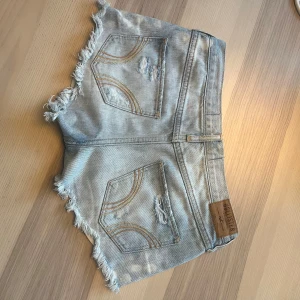 Ljusblå slitna jeansshorts Hollister - Säljer ett par ljusblå jeansshorts från Hollister med slitna detaljer och fransiga kanter. Shortsen har klassiska fickor bak med gulddetaljer och logga framtill. Perfekta för sommaren och ger en avslappnad vibe. Midjemått: 38 cm rakt över! Var snabba många intresserade därav pris!! 