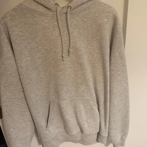 Grå hoodie från BikBok med huva - Mysig grå hoodie från BikBok i storlek M. Klassisk modell med huva, snörning och stor känguruficka framtill. Perfekt för chill dagar och enkel att matcha med jeans eller leggings. Tillverkad i mjuk bomullsblandning för extra komfort.