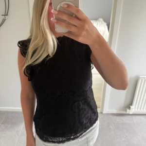 Svart spetsblus med volangärm - Supersnygg svart blus i spets med fina volangdetaljer vid ärmarna som man knäpper i nacken.❤️‍🔥köpt från Zalando