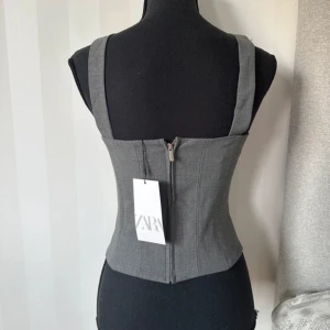 Grå korsettopp från Zara - Snygg grå korsettopp från Zara med breda axelband och markerad midja. 