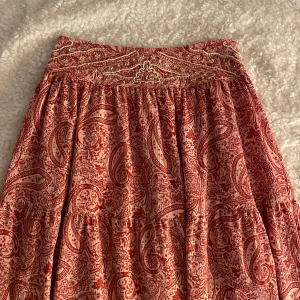 Röd paisleymönstrad långkjol från Zara - Superfin långkjol från Zara i rött och vitt med paisleyinspirerat mönster och broderade pärldetaljer i midjan. Kjolen har en luftig och flowy passform, perfekt för varma dagar. Resår i midjan för extra komfort.