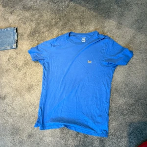 Blå t-shirt från Lee i bomull - Enkel blå t-shirt från Lee med liten logga på bröstet. Klassisk rund halsringning och normal passform. Perfekt basic-plagg i mjuk bomull som funkar till allt.