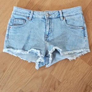 Ljusblå jeansshorts från H&M Divided - Snygga ljusblå jeansshorts från H&M Divided i storlek 36. Modellen är klassisk femficksdesign med fransiga kanter och råa benslut för en avslappnad vibe. Perfekta för varma dagar och enkel att matcha med allt. Materialet är mjukt denim.
