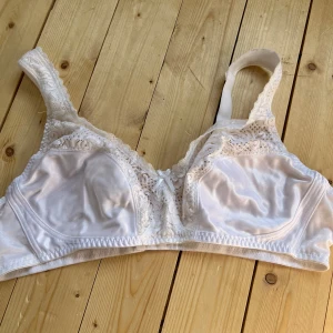 Vit spets-bh från Trofé 105B - Säljer en vit bh från Trofé i storlek 105B. Bh:n har vackra spetsdetaljer upptill och en liten rosett framtill. Axelbanden är breda och bekväma, och materialet är mjukt och glansigt. Perfekt för dig som gillar klassisk och feminin stil.