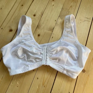 Vit linnetopp från Glamorise - Säljer en vit linnetopp från Glamorise med breda axelband och snygg rynkdetalj framtill. Toppen har hakknäppning fram och är tillverkad i ett glansigt, mjukt material som känns bekvämt mot huden. Perfekt för dig som vill ha en enkel och stilren look.