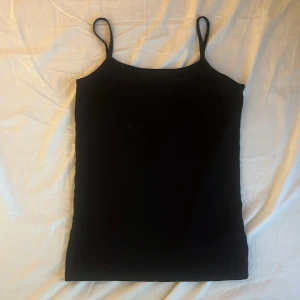 Svart linnetopp från Basic You - En svart, enkel och stilren linnetopp från Basic You i ekologisk bomull. Toppen har smala axelband och rak passform, perfekt att matcha med jeans eller kjol. Mjuk och skön mot huden tack vare materialet i bomull.