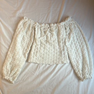 Vit offshoulder spetsblus från Nelly - Superfin vit offshoulder blus från Nelly i spets med puffiga långa ärmar och knytning framtill. Toppens tyg har ett diskret mönster och är lätt transparent, perfekt för en trendig look. Resår vid axlar och ärmslut ger en snygg passform. Nypris 399 kr.