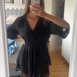 Svart kort omlottklänning med struktur - Säljer en jätte fin svart mönsterklänning som funkar bra till allt. Har använt på vintern och sommar kvällar 