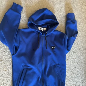 Blå Comme des Garçonst Play hoodie (CDG) - Säljer en blå hoodie från Comme des Garçons Play (CDG) Tröjan har det ikoniska svarta hjärtat med ögon på bröstet och en stor version på ryggen. skön passform. Storlek L passar M också.    Säljer den för att jag inte använder den längre:) priset är prutbart…