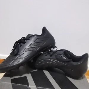 Svarta Adidas Copa fotbollsskor - Helt by aldrig använts. Låda finns. Snygga helsvarta Adidas Copa fotbollsskor med klassisk design och tre diskreta ränder på sidan. Skorna har snörning och är tillverkade i syntetmaterial för en lätt känsla på planen. Perfekta för dig som vill ha stilrena och funktionella skor till matchen.