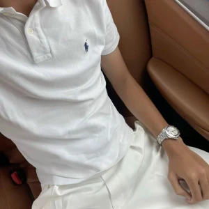 Vit pikétröja från Polo Ralph Lauren - Klassisk vit pikétröja från Polo Ralph Lauren med broderad marinblå logga på bröstet. Tröjan har korta ärmar, krage och knäppning med tre knappar. Tillverkad i mjuk bomull som känns fräsch och passar perfekt till stil .