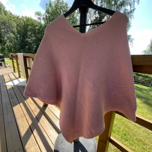 Ljusrosa stickad poncho från KappAhl - Superfin ljusrosa stickad poncho från KappAhl. Den har en snygg v-ringning och är tillverkad i mjuk bomull och polyester. Perfekt att slänga över en t-shirt eller långärmad för en chill look. Oversized och flowig passform.
