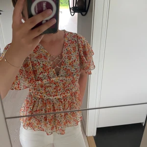 Blommig blus med snörning från Zara - Supersöt blommig blus från Zara Basic med volangärmar och v-ringning med snörningsdetalj framtill. Topp i tunn, luftigt material med små blommor i orange, rött och gult på vit botten. Perfekt för vår och sommar💛💛💛