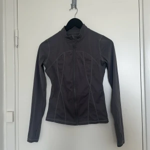 Grå träningsjacka med dragkedja - Grå träningsjacka med dragkedja. Jackan har en tight passform och långa ärmar.