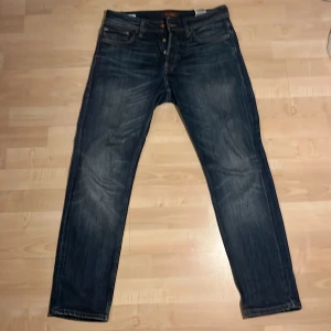 Blå jeans från Jack & Jones - Snygga blå jeans från Jack & Jones med klassisk femficksdesign och dragkedja. Perfekta för en avslappnad stil. Midjemått 30.