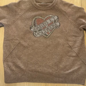 Brun stickad tröja från Zadig & Voltaire - Säljer en brun stickad tröja från Zadig & Voltaire med ett stort hjärtmotiv på framsidan. Tröjan har ribbade kanter och subtila mönster vid sidorna. Tröjan är jättemjuk och har 65 % ylle. Perfekt för en stilren och unik look. ❤️