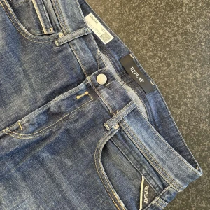 Blå jeans från Replay - Snygga blå jeans från Replay med klassisk femficksdesign och knappgylf. Jeansen har en modern passform och är perfekta för en snygg stil. Märkesdetaljer syns på bakfickan och linningen. NY skick 10/10 (W29 L32)