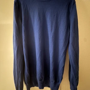 Merino ull tröja från J.Lindeberg - Säljer en stilren blå tröja från J.Lindeberg. Tröjan har en klassisk rund hals och långa ärmar. Perfekt för en avslappnad men ändå snygg look. Den är tillverkad i merino ull som är ett exklusivt material som sitter väldigt skönt mot huden. Nypris 1300. Säljer då den är för liten. Lite mindre i storleken. (Självklart hänger den inte på galge i vanliga fall eftersom det ”hänger ut” tröjan. Enbart för en bra helhetsbild).