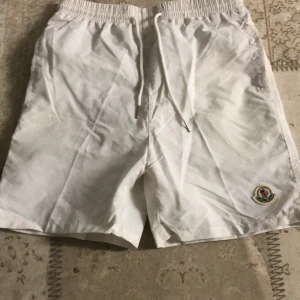 Vita shorts från Moncler - Snygga vita shorts från Moncler med elastisk midja och snörning. De har en broderad Moncler-logga på benet och en bakficka med knapp. Perfekta för en stilren look. 