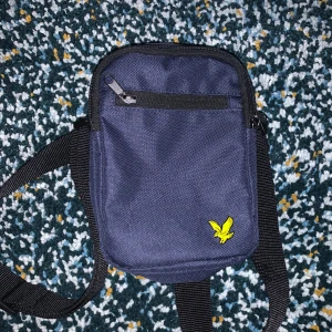 Lyle and scott axelväska  - Snygg blå axelväska från Lyle and scott. Väskan har 3 fack. Perfekt för att bära med sig det nödvändigaste.
