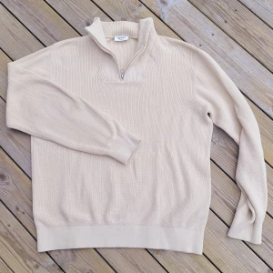 Beige stickad tröja från Kappahl - Säljer en stilren beige stickad tröja från Kappahl med dragkedja vid halsen. Tröjan har långa ärmar och ribbade muddar vid ärmslut och nederkant.