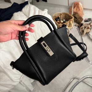 Svart handväska med axelrem - Snygg svart handväska i skinn med en justerbar axelrem och ett elegant lås framtill. Perfekt för att bära dina nödvändigheter med stil. Väskan har en stilren design och är lätt att matcha med olika outfits. 🌺 #ginatricot