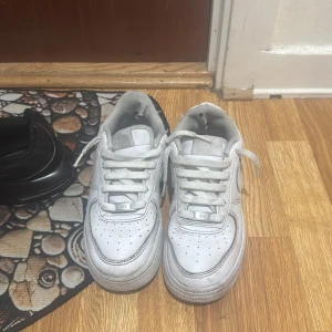 Vita Nike Air Force sneakers - Säljer ett par klassiska vita Nike Air Force sneakers. De har en stilren design med snörning och en bekväm passform. Perfekta för en casual look.