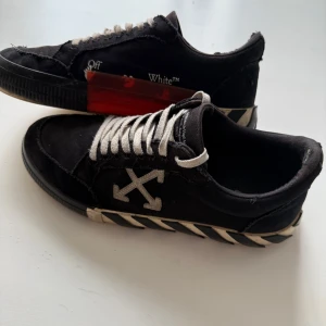  Off-White sneakers - Snygga svarta sneakers från Off-White storlek 42 med vita snören och ikoniska pilar på sidan. Skorna har en unik design med textdetaljer och en röd accent på sulan. Perfekta för den stilmedvetna.
