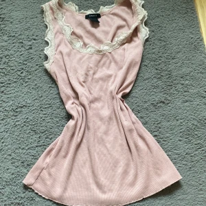 Rosa ribbad topp från Lindex - Säljer en söt rosa ribbad topp från Lindex med vackra spetsdetaljer runt halsringningen och ärmarna. Perfekt för en sommardag. Toppen är ärmlös och har en mjuk och bekväm passform.