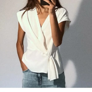 Vit omlottblus Zara - Vit omlottblus med korta ärmar och knytning i sidan. Perfekt för en elegant och avslappnad look. Aldrig använd.