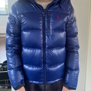Blå dunjacka från Ralph Lauren - Säljer en snygg blå dunjacka från Ralph Lauren med en klassisk pufferdesign. Jackan är helt oanvänd med etiket kvar. Bild 1 och 2 är modellen 180 cm och på bild 3 och 4 är modellen 188 cm. Bara att ställa frågor och pris kan diskuteras. 