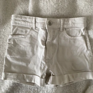 Vita jeansshorts storlek 134 - Snygga vita shorts med uppvikta ben. Perfekta för varma sommardagar. De har en knapp och dragkedja framtill för enkel påklädning. Superfint skick. Inga hål. Inga fläckar. 