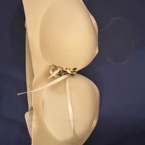 Beige axelbandslös bh - Säljer en beige axelbandslös bh med knytning framtill. Perfekt för klänningar och toppar utan axelband. Den har en slät yta och justerbara band för bästa passform.