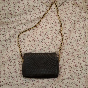 Svart quiltad axelväska med kedja - Snygg svart axelväska med quiltad design och guldfärgad kedja. Väskan har en praktisk dragkedja inuti och stängs med en tryckknapp. Perfekt för att ge en elegant touch till din outfit. Endast avänd ca 5 gånger. Pris kan diskuteras! 