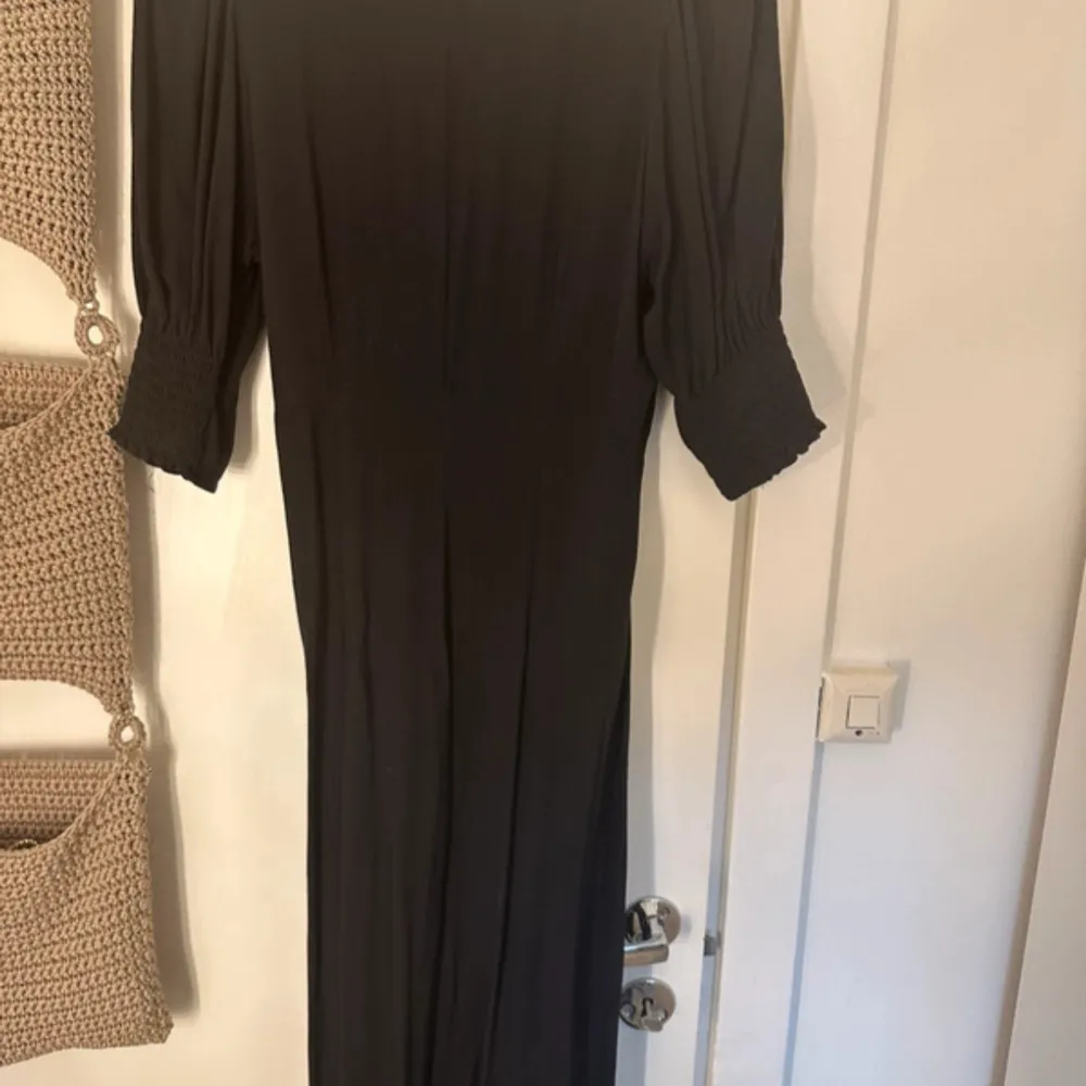 Elegant svart långklänning med v-ringad omlott-design och korta puff ärmar . Perfekt för en stilren look.. Mekot.