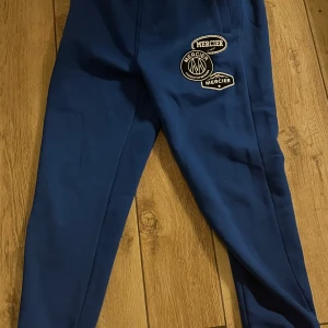 Blå mjukisbyxor från Mercier - Snygga blå mjukisbyxor från Mercier med broderade logotyper på sidan. Byxorna har en normal passform och är perfekta för en avslappnad stil. De är tillverkade i ett mjukt material som ger hög komfort.