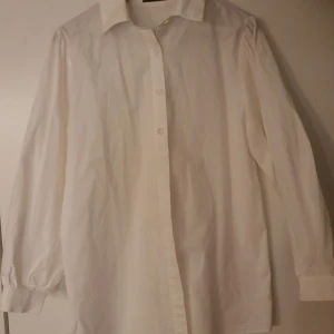 Vit långärmad skjorta - Klassisk vit skjorta med långa ärmar och knappar framtill. Perfekt för en stilren look.