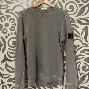 Beige långärmad tröja från Stone Island - Säljer en stilren beige långärmad tröja från Stone Island. Tröjan har en rund halsringning och synliga sömmar som ger en cool look. Stone Island-loggan sitter på ärmen. Skriv för fler bilder, org pris 2500kr