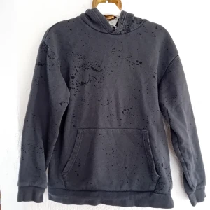Mörkgrå hoodie med mönster - Säljer en mörkgrå hoodie med ett unikt stänkmönster. Tröjan har en klassisk känguruficka och en bekväm huva. Perfekt för en avslappnad stil.