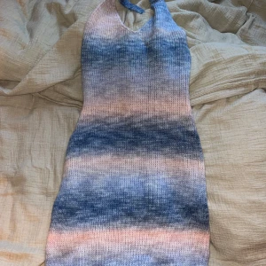Stickad klänning i blå och rosa toner - Säljer en stickad klänning med vackra övergångar i blå och rosa toner. Klänningen har en halterneck-design och är ärmlös, vilket ger en somrig känsla. Perfekt för en avslappnad dag ute eller en mysig kväll hemma.