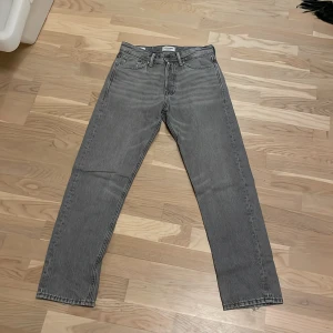 Grå jeans från Jack & Jones - Snygga grå jeans från Jack & Jones med klassisk femficksdesign. De har en rak passform och är tillverkade i slitstarkt denim. Perfekta för en stilren look.