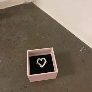 Silverfärgad ring med hjärta - Säljer en stilren silverfärgad ring med ett hjärta i mitten. Perfekt för att ge en subtil men elegant touch till din outfit 