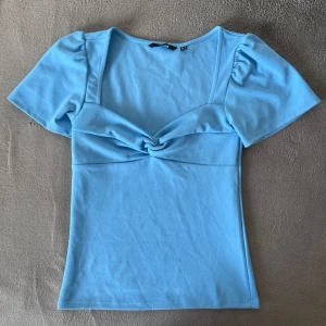 Blå topp från Vero Moda - Säljer en snygg blå topp från Vero Moda med korta ärmar och en knytdetalj framtill. Perfekt till våren🩵