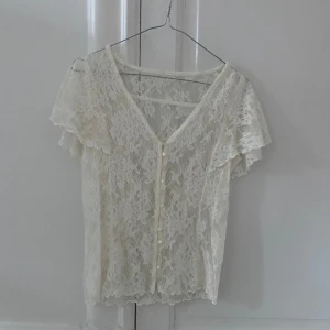Vit spetsblus med knappar - Säljer en elegant vit spetsblus med korta ärmar och v-ringning. Blusen har fina knappar framtill och ett romantiskt utseende. Perfekt för en somrig look eller en speciell tillställning.