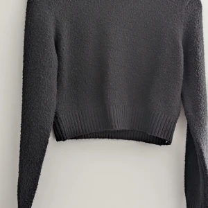 Svart stickad tröja från Sister Knitwear - Mysig svart stickad tröja från Sister Knitwear i storlek S. Tröjan har en croppad passform, långa ärmar och ribbad nederkant. Perfekt för lager-på-lager och passar till både jeans och kjol. Säljer då jag inte kan ha svart i hemmet för katter.
