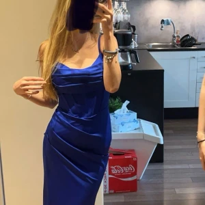 Kornblå långklänning med smala axelband - Supersnygg långklänning i kornblått med smala axelband och draperad omlott vid bysten. Klänningen har figurnära passform och elegant fall. Perfekt för dig som vill sticka ut med en färgstark look. Materialet känns slätt och har ett fint lyster.