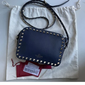 Mörkblå Valentino väska (camerabag) - Säljer en mörkblå Valentino camerbag i mycket bra skick. Den är mörkblå och passar till allt, perfekt till många tillfällen. Har dustbag, äkthetsbevis och extra nitar! Kan mötas upp i Sthlm!💗💗💗kan tänka mig byta till annan väska, till exempel annan modell på valentino, ysl osv