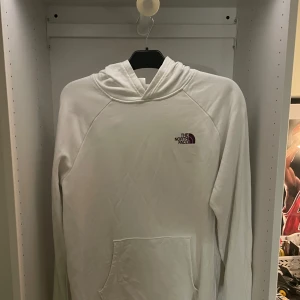 Vit hoodie från The North Face  - Säljer en vit hoodie från The North Face i storlek L. Tröjan har stor logga och texten 'Never Stop Exploring' på ryggen, samt mindre logga på bröstet. Klassisk känguruficka framtill och huva. Perfekt för dig som gillar streetwear och enkel stil. Aldrig använd